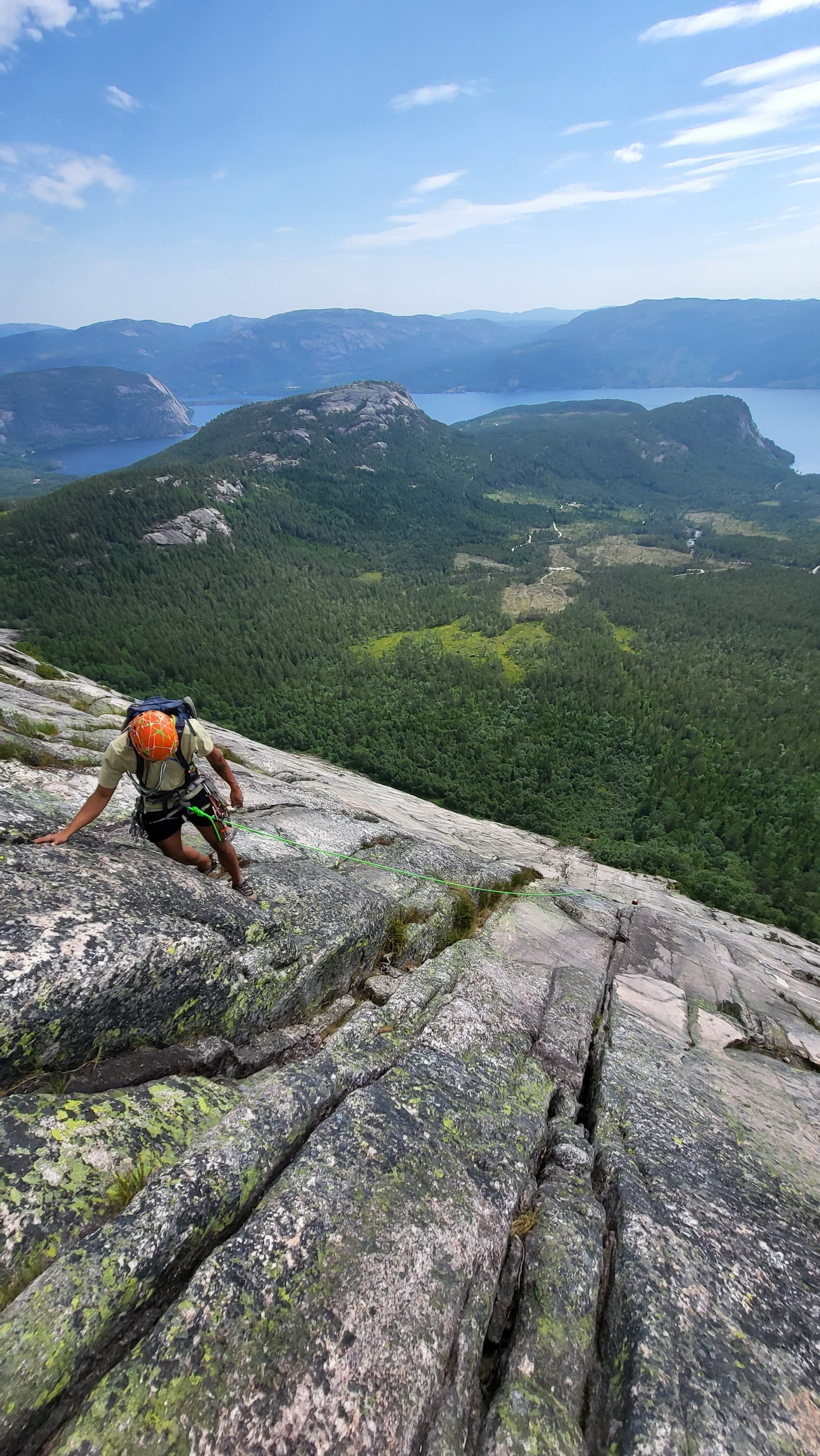 A climber on a granite slab above forest and lakes