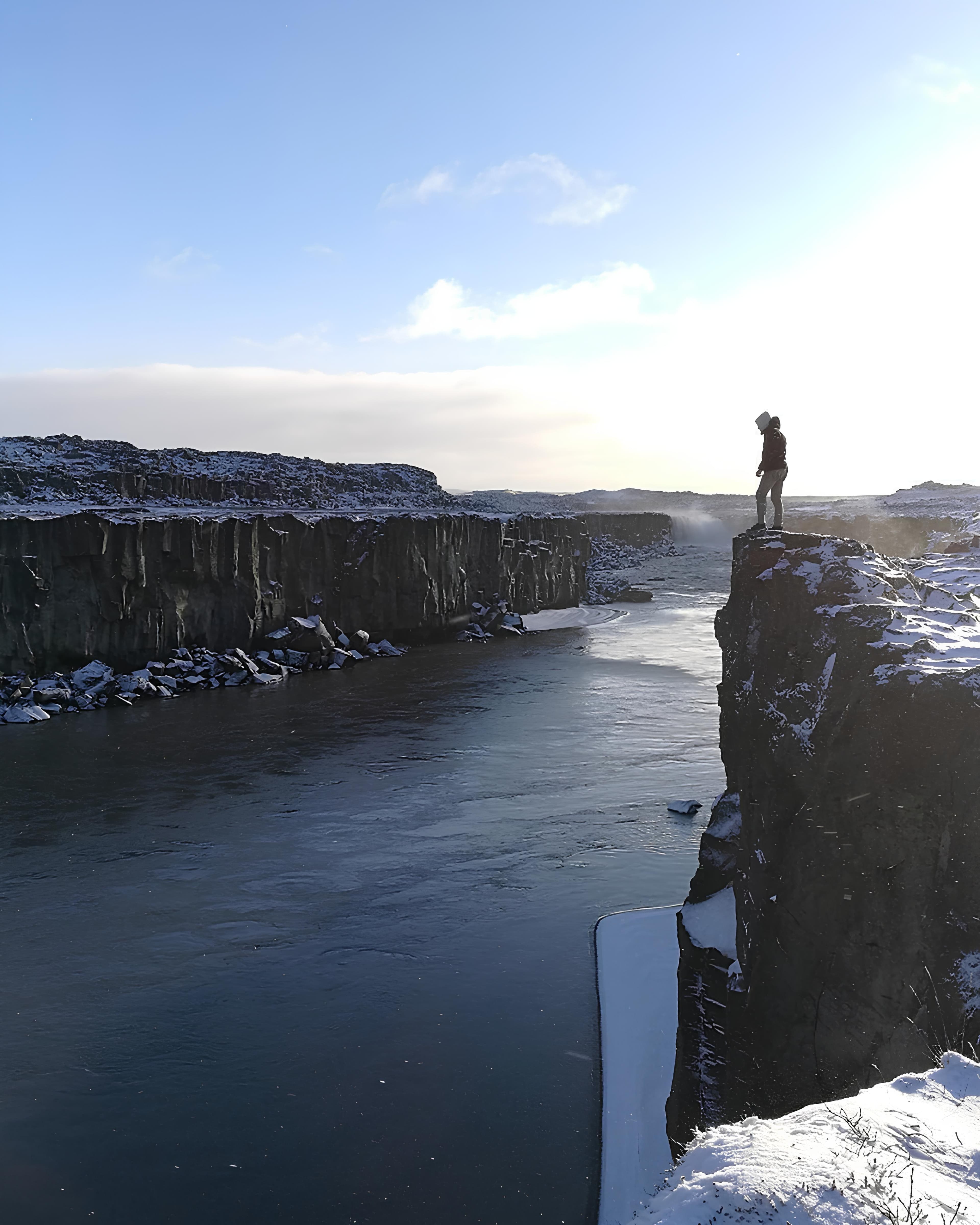A person standing on a snowy cliff above a winter river canyon