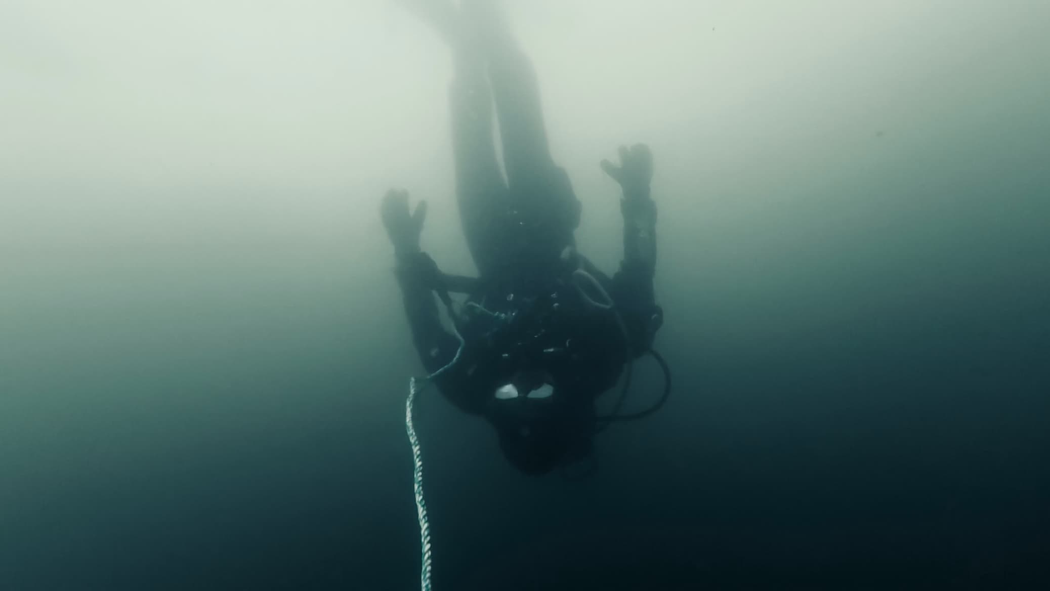 A scuba diver descending a line in green-blue water