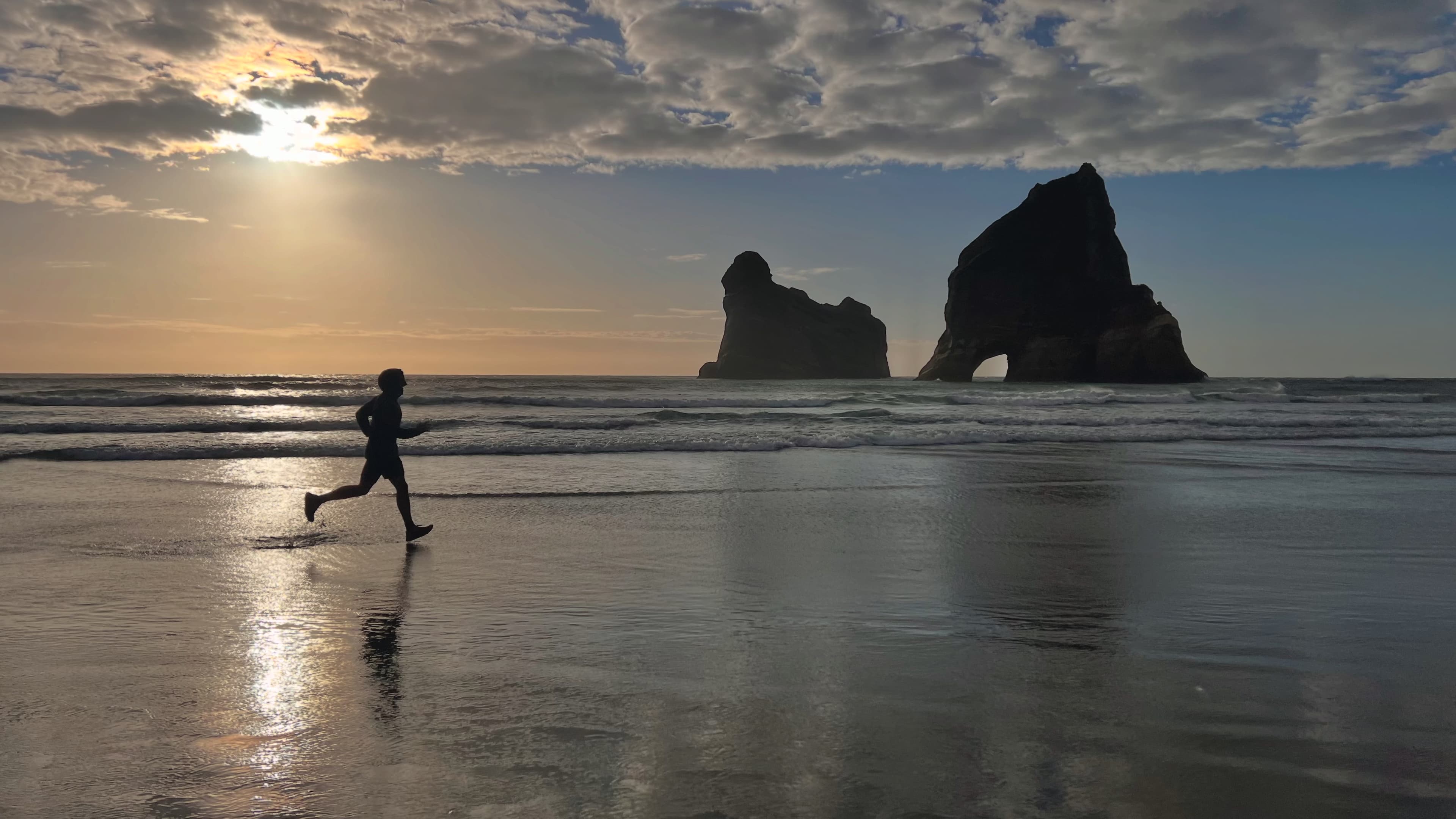 A runner on a wet beach at sunset beside sea stacks