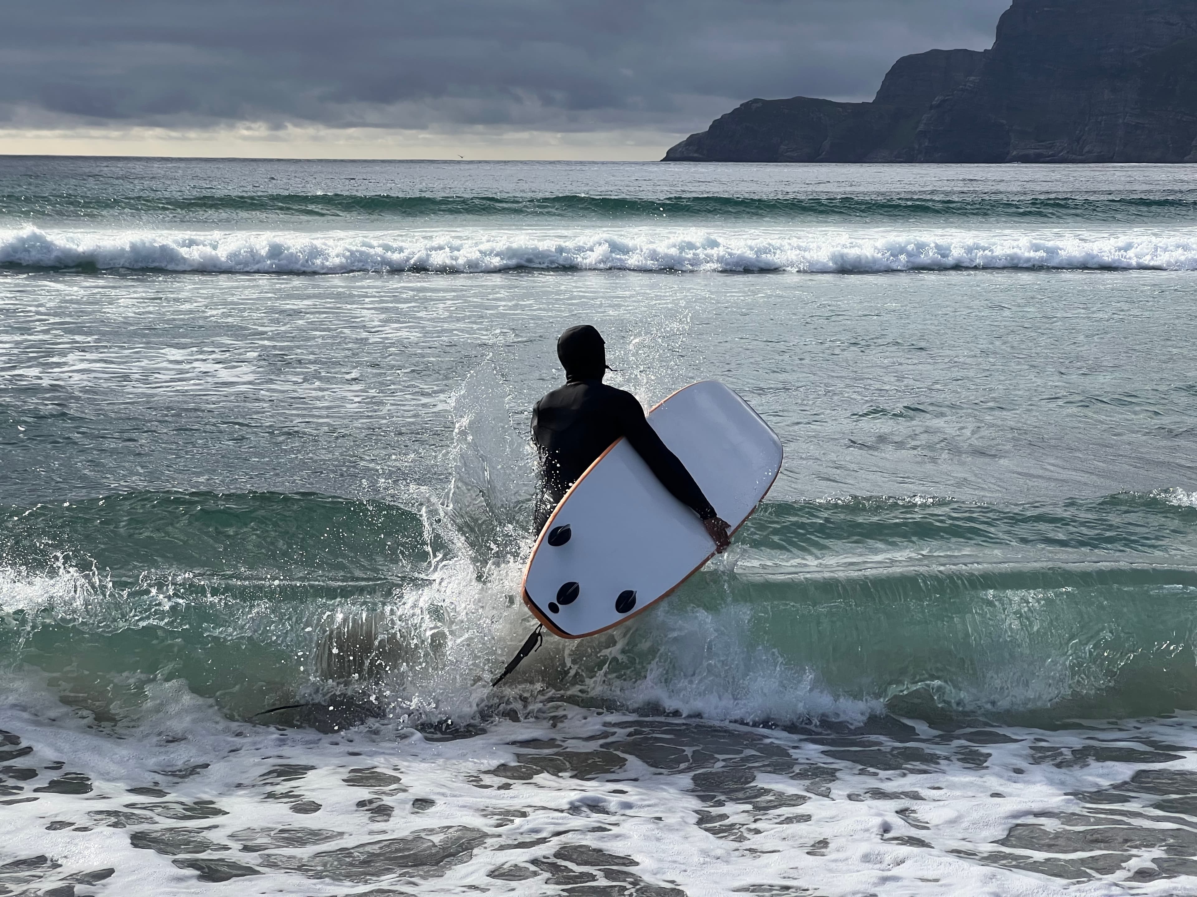 A surfer in a wetsuit carrying a board into breaking waves